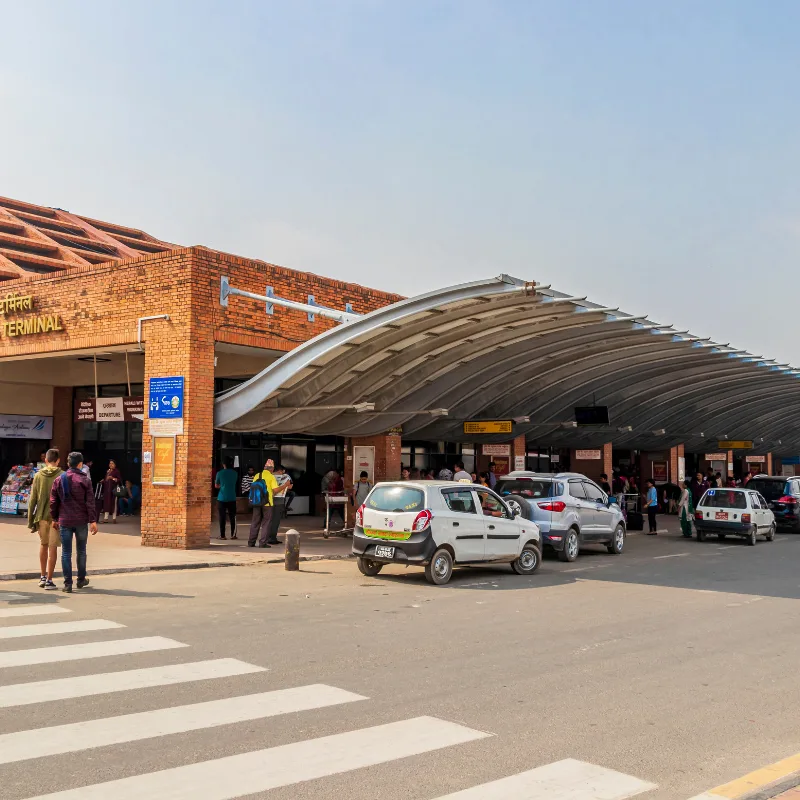 Exterior view of the brick departure terminal and canopy with taxis and travelers at Tribhuvan International Airport Kathmandu Nepal.