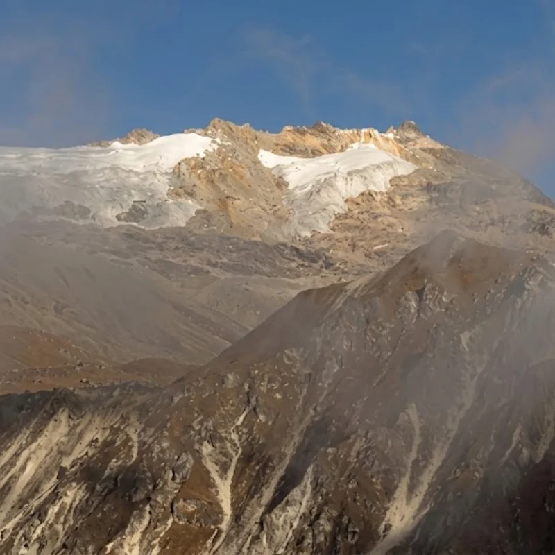 Rugged Himalayan mountain peaks and glacier covered with light snow under a clear blue sky.