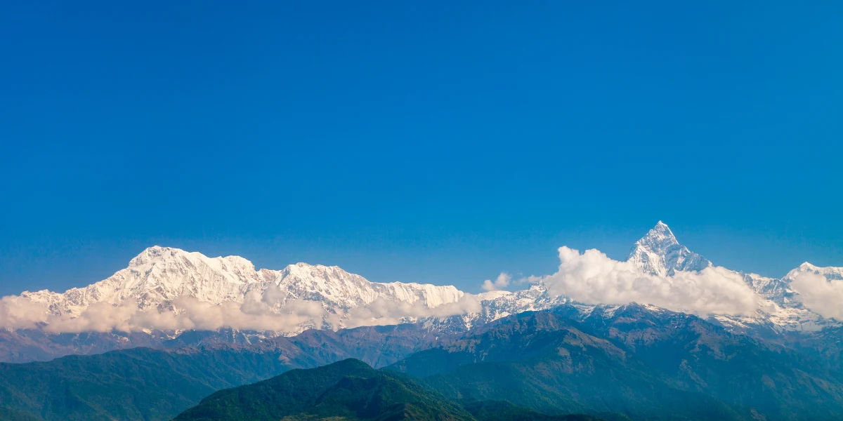 Wide panoramic view of the snow-capped Annapurna mountain range and Fishtail peak under a clear blue sky in Nepal.