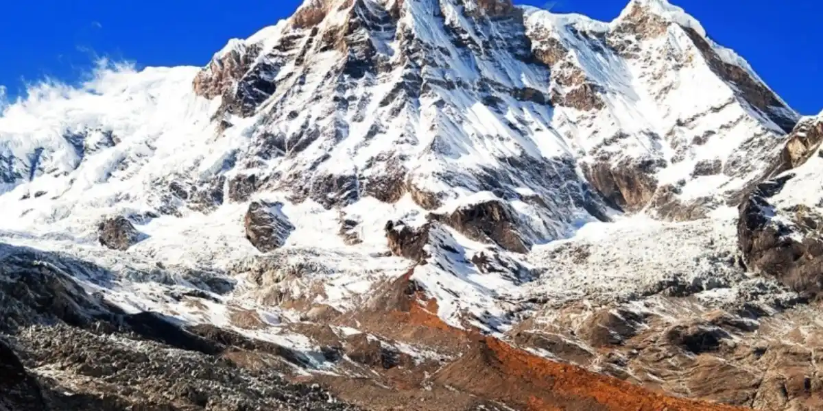 Massive, snow-covered rock wall of Mount Annapurna South rising steeply into a vibrant blue sky in Nepal.